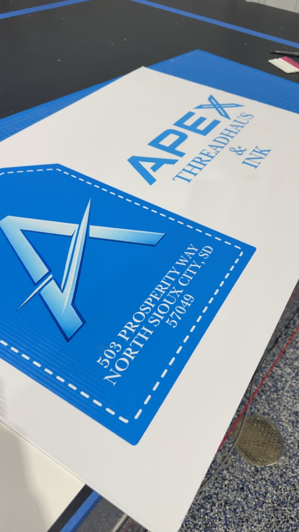 White and blue Apex Threadhaus & Ink yard sign with the shop’s logo and address